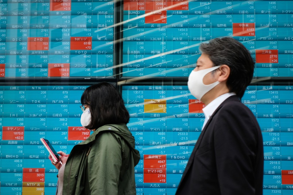 Pedestrians walk past a board displaying stock prices on the Tokyo Stock Exchange. Photo: AFP