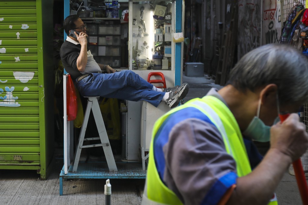 A man puts his feet up as he talks on the phone in Wan Chai on December 7 while a street cleaner works nearby. The lack of respect and compensation afforded to street cleaners and other essential workers is one of the many inequities highlighted by the pandemic. Photo: K.Y. Cheng