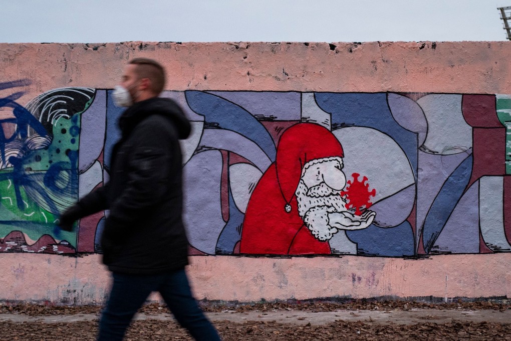 A man wearing a face mask walks past a mural in Berlin featuring a likeness of Santa Claus holding a coronavirus. Photo: AFP
