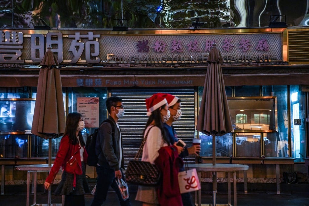 People wearing protective masks and Santa hats walk past a closed restaurant in Tsim Sha Tsui on December 24. The restrictions on restaurant service as the city struggles to contain the spread of Covid-19 has hit the food and beverage sector hard at what is usually a profitable time of the year. Photo: Bloomberg