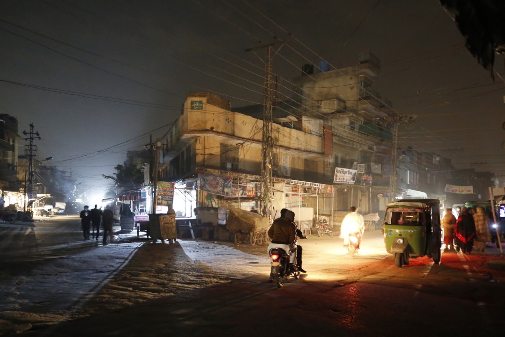 People are silhouetted on vehicle headlights on a dark street during widespread power outages in Rawalpindi, Pakistan. Photo: AP