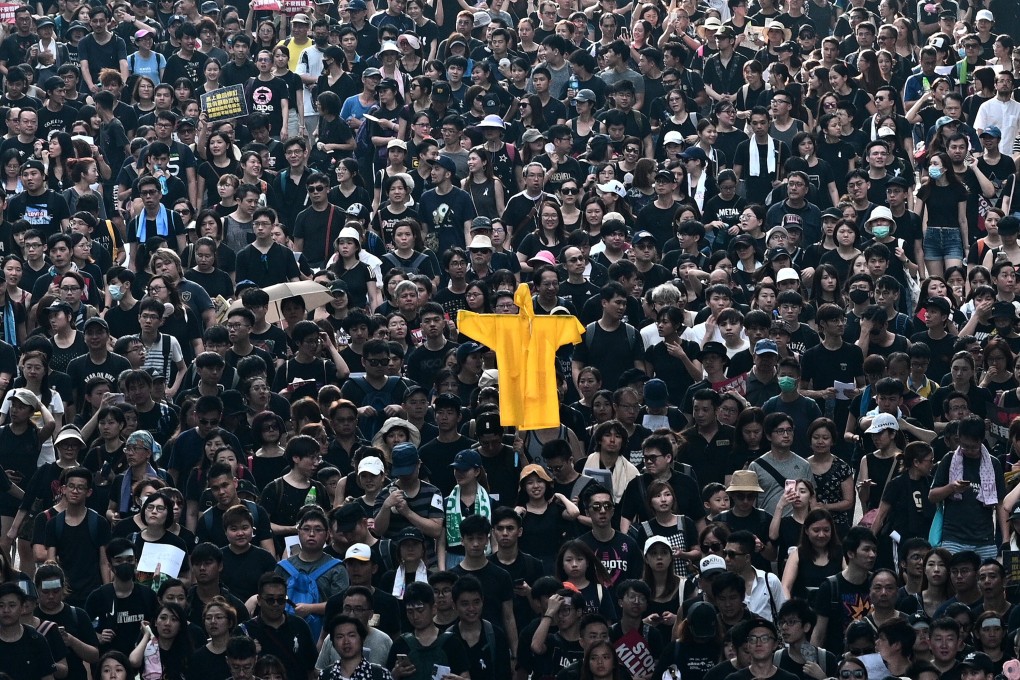 People are seen in Hong Kong on June 16, 2019, holding up a yellow raincoat in memory of a fellow protester who fell to his death during an earlier demonstration. Photo: AFP