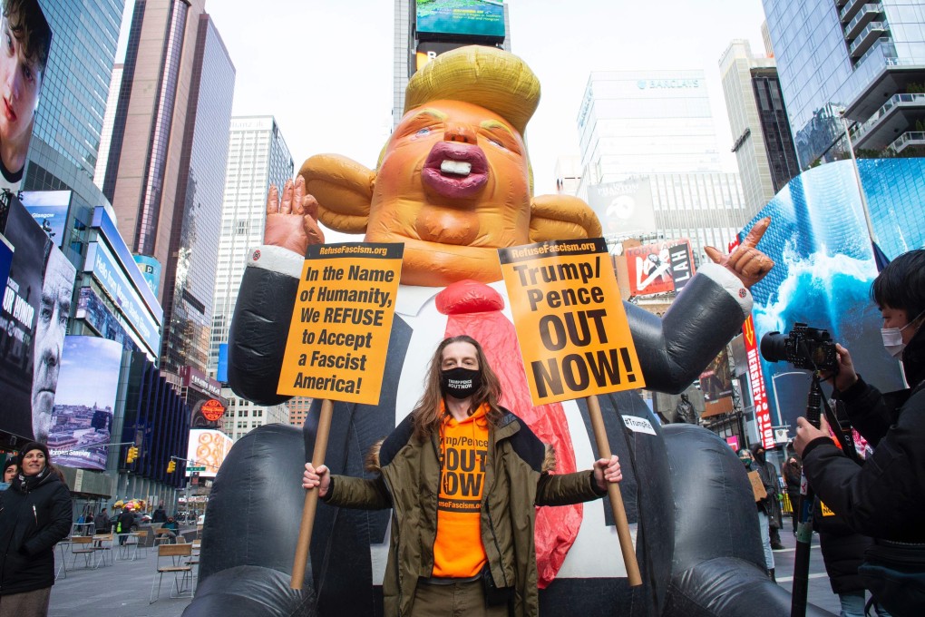 A protester poses with posters next to a Donald Trump Rat Balloon created by local artists during a demonstration in Times Square, New York on January 9. Photo: AFP