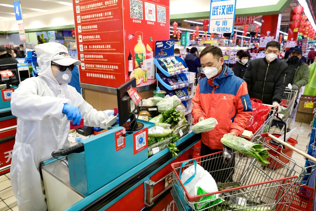 A worker in protective suit serves customers at a supermarket checkout counter in Wuhan in February 2020, amid the coronavirus outbreak. Photo: China Daily via Reuters