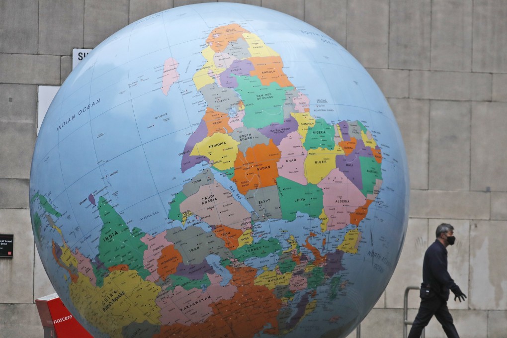 A man wearing a face mask walks past a globe in front of the London School of Economics in London. Photo: AP