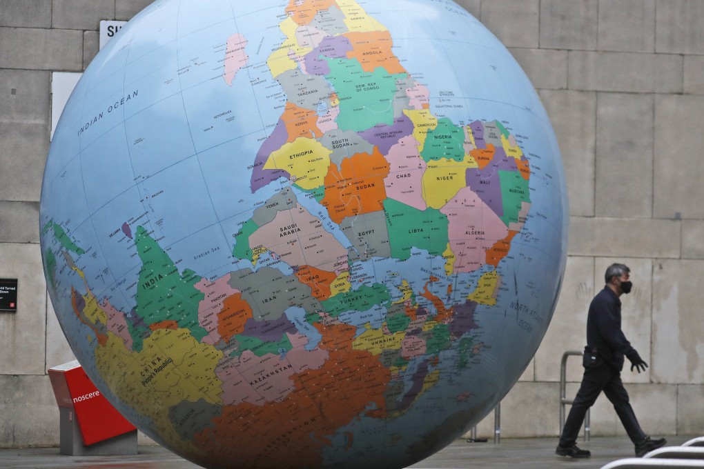 A man wearing a face mask walks past an upside-down globe in front of the London School of Economics in London on Tuesday. Photo: AP