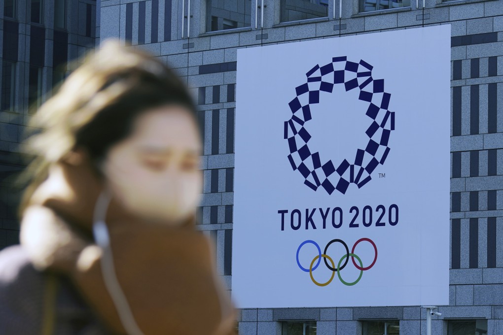 A woman wearing a protective mask to help curb the spread of the coronavirus walks near a banner of the Tokyo 2020 Olympics in Tokyo this month. Photo: AP.