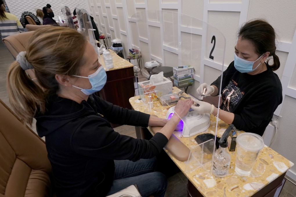A nail technician sits behind a plexiglass shield as she gives a manicure to a customer in California. Photo: AP