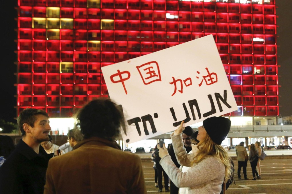 A woman holds a placard to support China in front of the Tel Aviv Municipality Hall lit up with the colours of China’s national flag in solidarity with China's fight against Covid-19, in Israel, on February 11, 2020. Photo: Xinhua