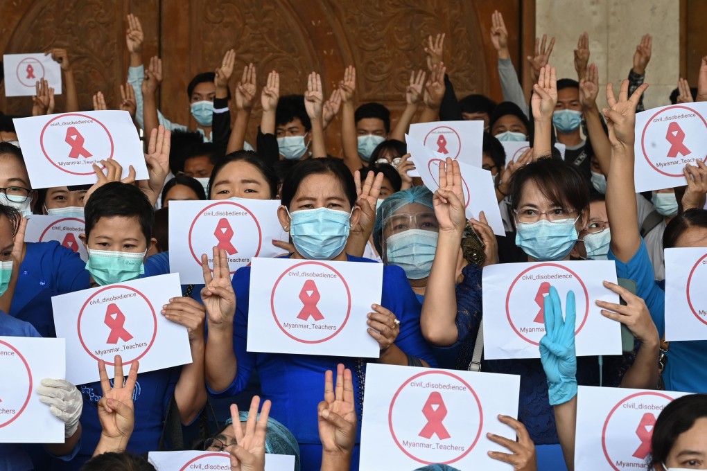 University teachers hold up three-finger salutes and signs with red ribbons calling for civil disobedience during a protest against the military coup at Dagon University in Yangon on Friday. Photo: AFP