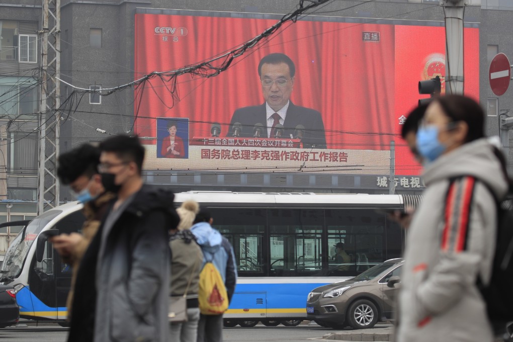 Pedestrians pass a screen showing Chinese Premier Li Keqiang speaking during the opening session of the National People's Congress in Beijing. Photo: EPA-EFE/STR
