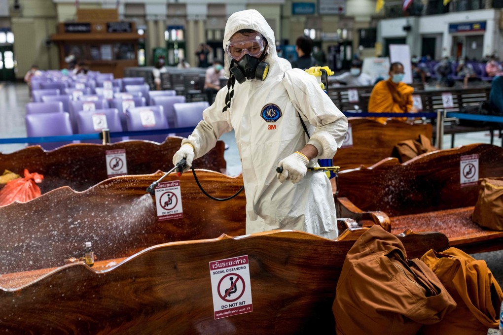 A cleaner wearing personal protective equipment sprays disinfectant on seats in Bangkok’s Hua Lamphong railway station. Photo: AFP
