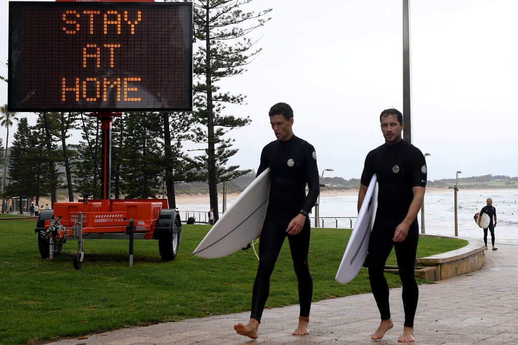 Surfers walk past a billboard urging people to stay at home, in Sydney on December 19, 2020. Photo: EPA-EFE