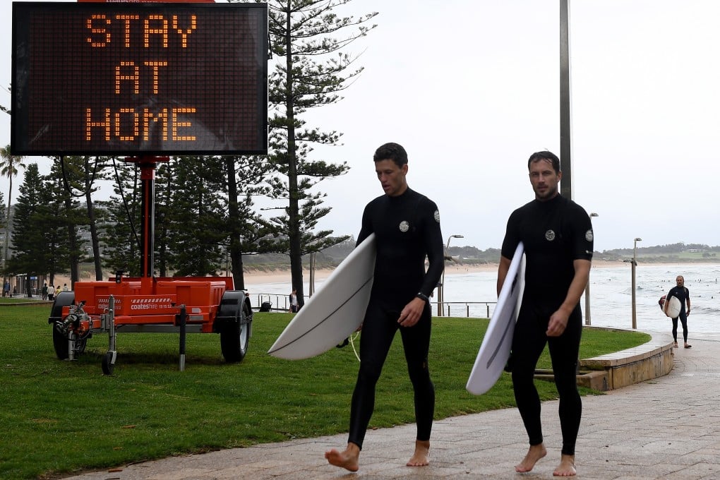 Surfers walk past a billboard urging people to stay at home, in Sydney on December 19, 2020. Photo: EPA-EFE