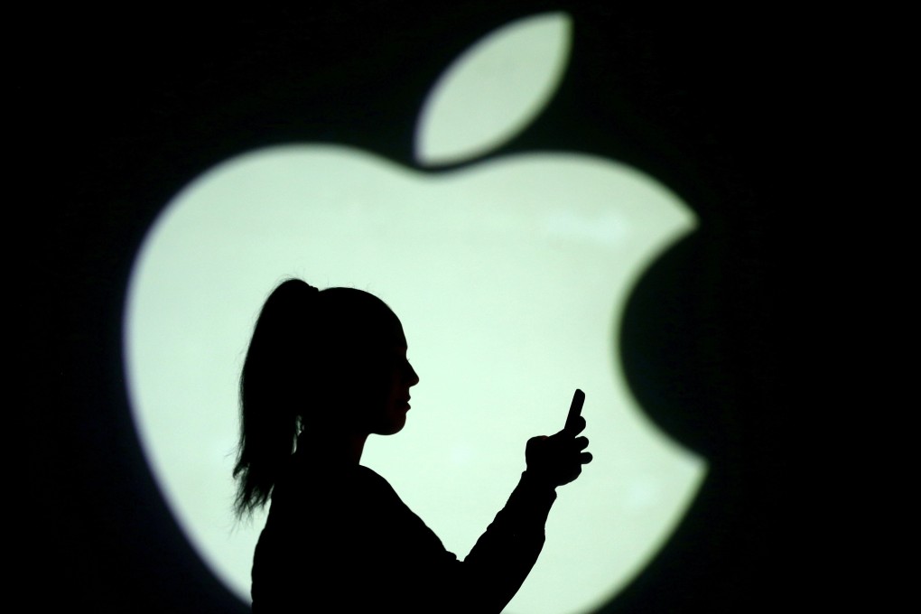Silhouette of a mobile user seen next to a screen projection of the Apple logo. Photo: Reuters