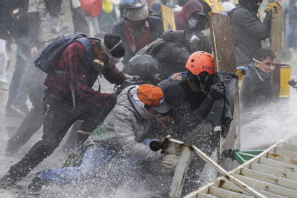 Anti-government protesters take cover from a police water cannon during clashes in Madrid, on the outskirts of Bogota, Colombia on May 28. Photo: AP