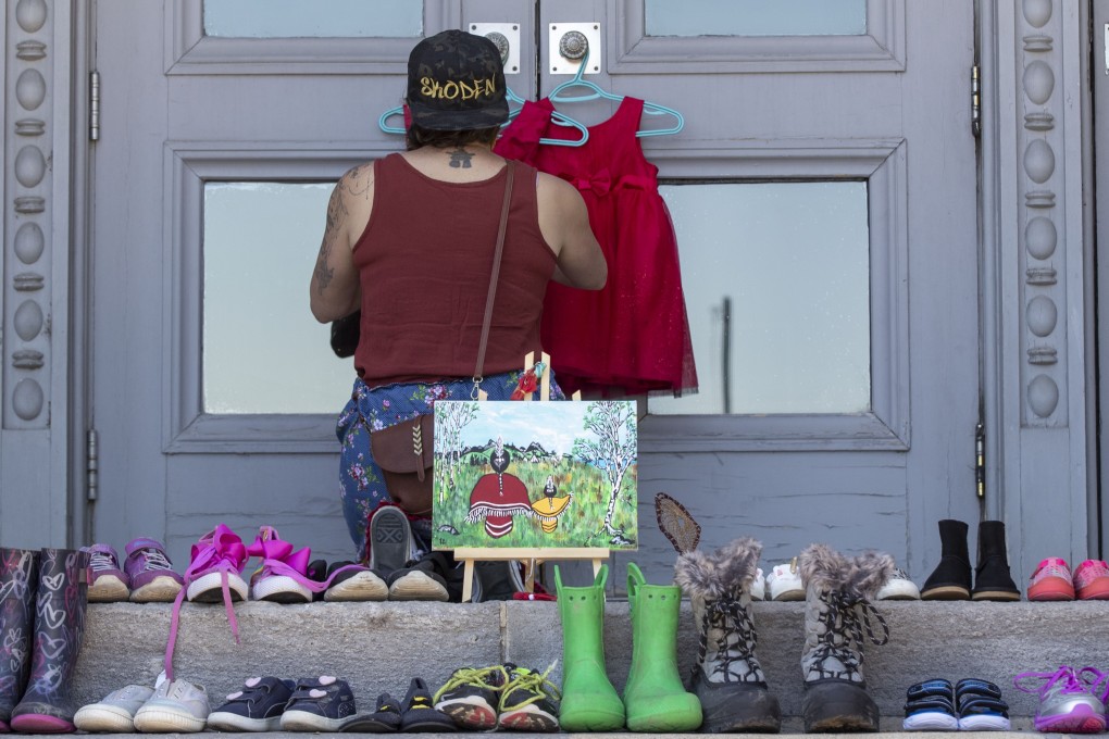 A person hangs red dresses beside shoes outside the City Hall in Kingston, Ontario. The remains of 215 children were recently discovered on the grounds of the former Kamloops Indian Residential School. Photo: AP