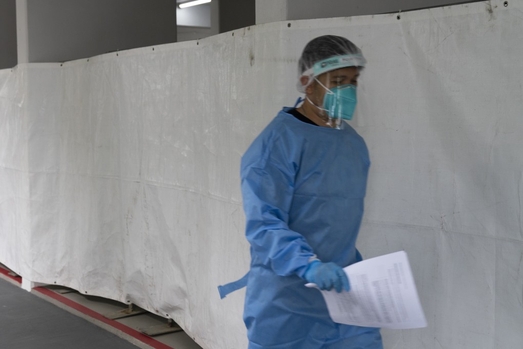A health care worker wearing personal protective equipment walks past a mandatory Covid-19 test site at a housing block in Singapore, amid a rise in new and unlinked infections. Photo: Bloomberg