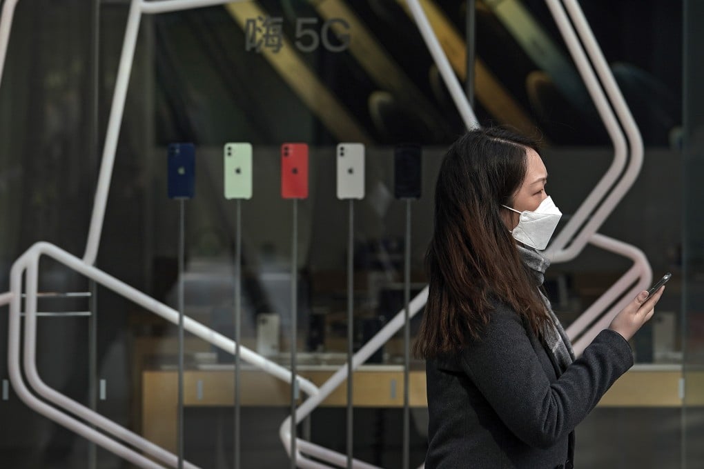 A woman holds her smartphone as she passes an Apple Store promoting the iPhone 12 in Beijing on February 24, 2021. Apple supplier Foxconn Technology Group is now bolstering production capacity at the world’s largest iPhone factory in the central Chinese city of Zhengzhou. Photo: AP