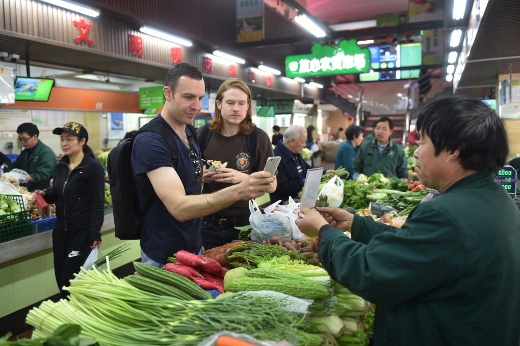 Tim Clancy (left) of Australia, a resident for six years in the Zhejiang provincial capital of Hangzhou, takes his American friend (centre) to a vegetable market where he pays for vegetables through mobile payment on April 14, 2017. Photo: Xinhua