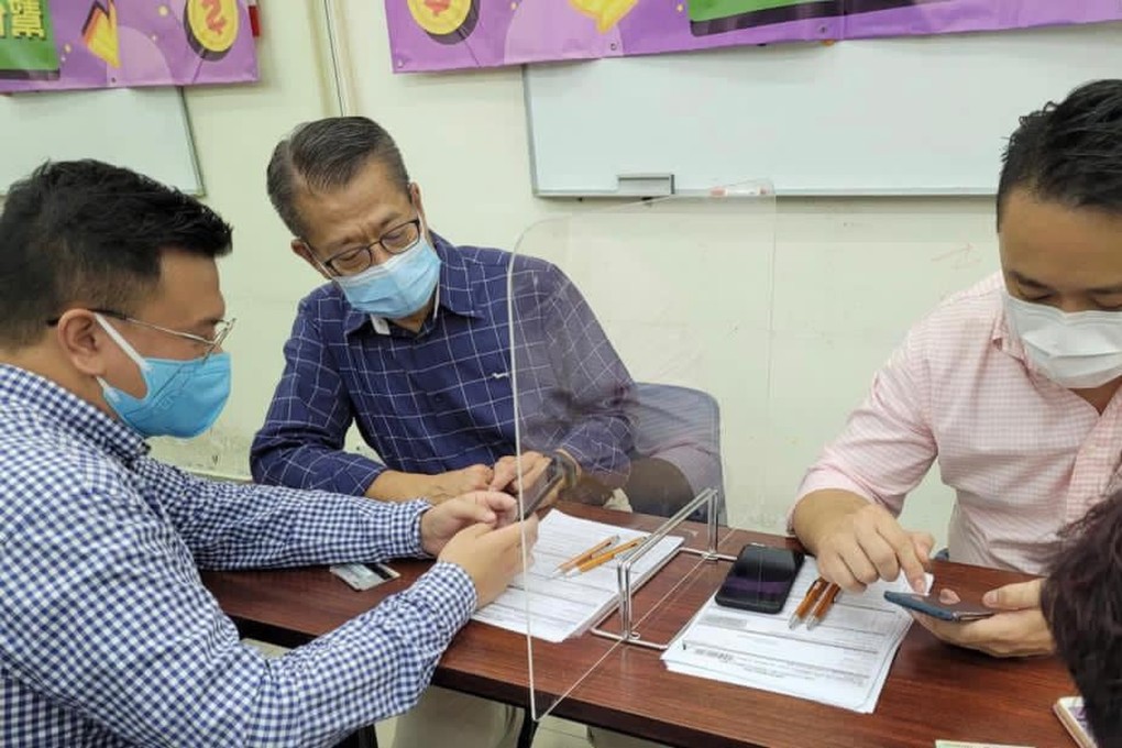 Financial Secretary Paul Chan (centre) helps someone register for the scheme. Photo: Facebook