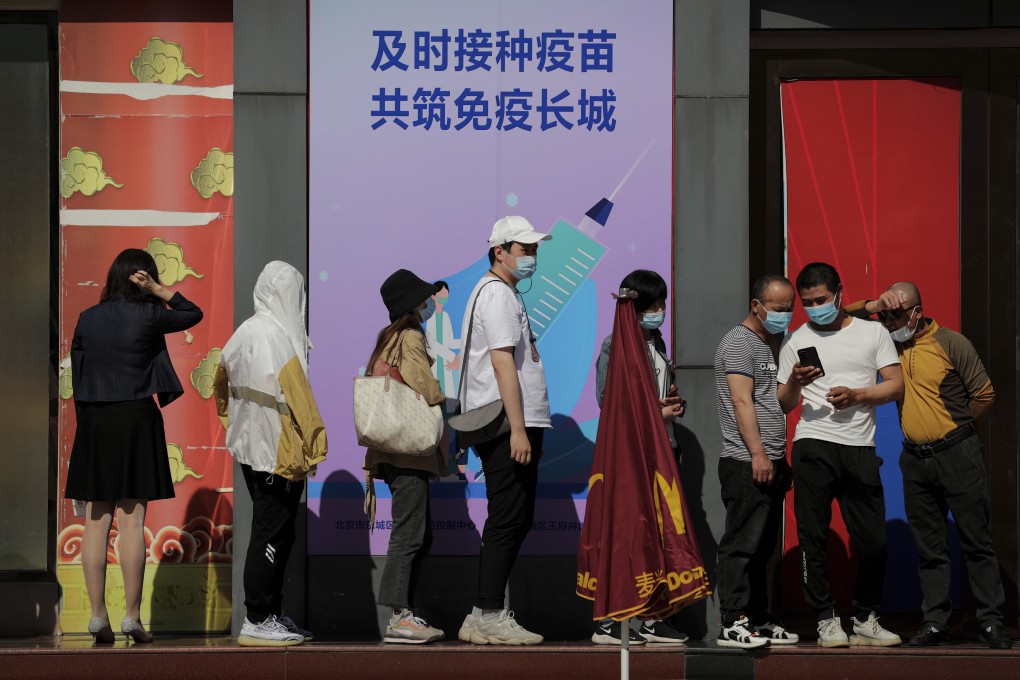 Beijing residents line up for vaccine shots below a board displaying the slogan, “Timely vaccination to build the Great Wall of immunity together.” Photo: AP