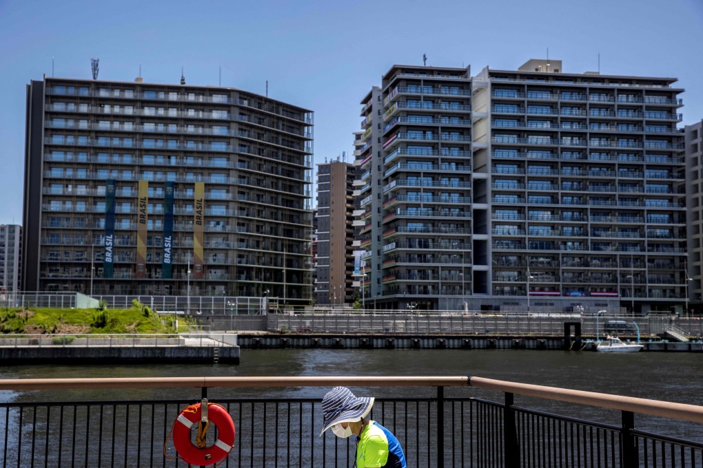 A woman sits on a bench across from the Tokyo 2020 Olympic Village in Tokyo on Sunday. Photo: AFP