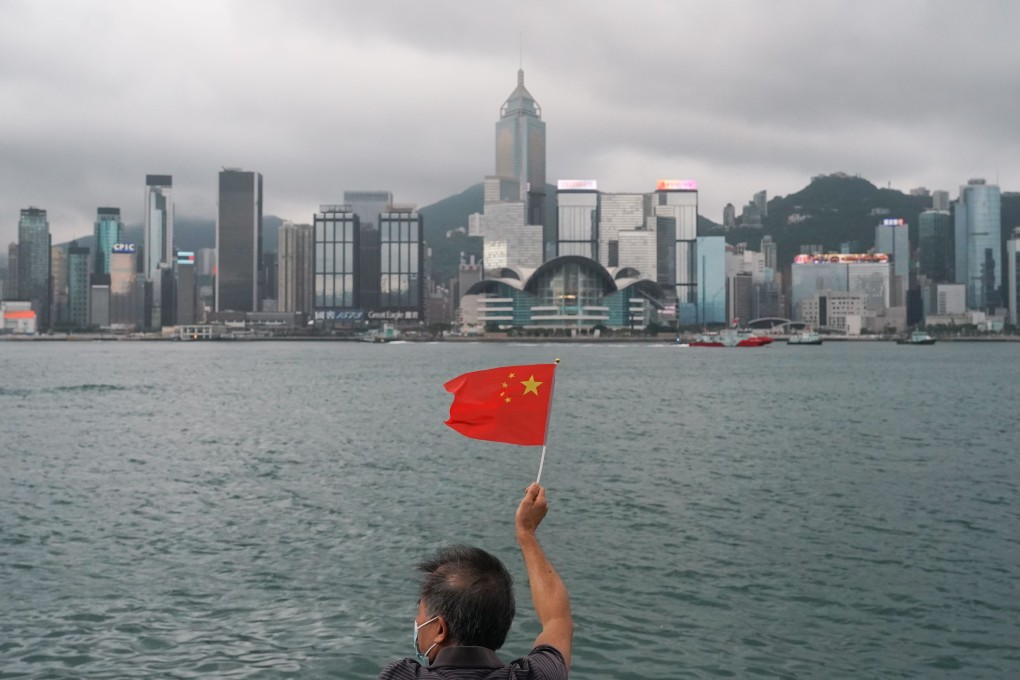 A man holds up the Chinese flag against the backdrop of Hong Kong’s iconic Victoria Harbour. Photo: Felix Wong