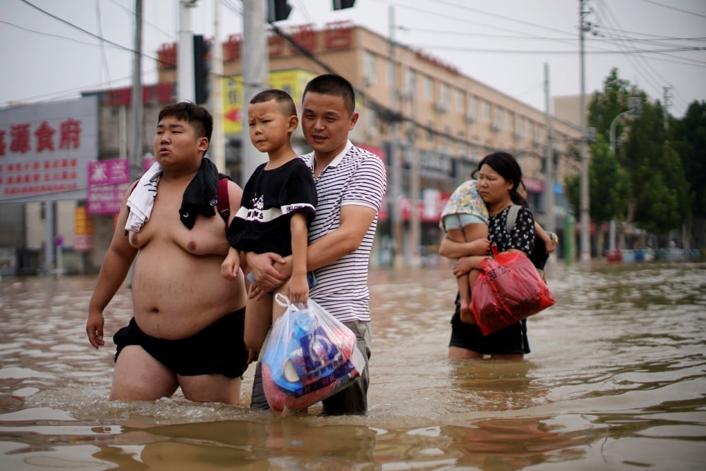 People carrying children and supplies wade through floodwater following record-breaking rainfall in China’s Henan province. Photo: Reuters