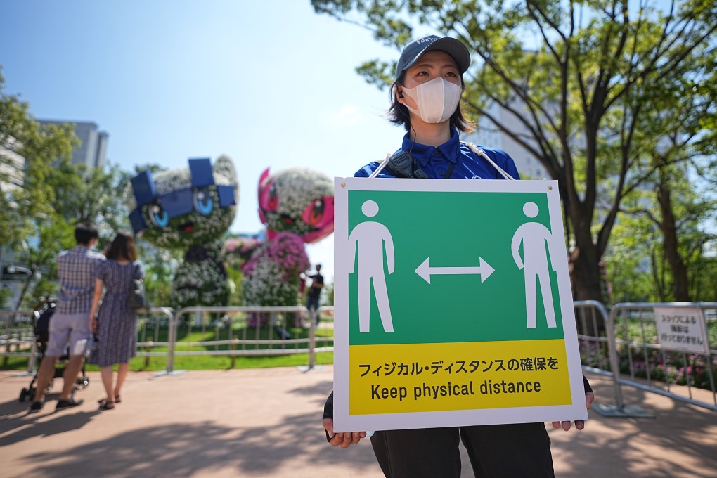 An Olympic Games staff member holds a sign with a symbol and the words “Keep physical distance” to ensure social distancing during the Games. Photo: DPA