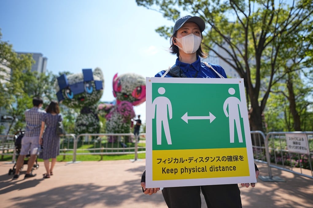 An Olympic Games staff member holds a sign with a symbol and the words “Keep physical distance” to ensure social distancing during the Games. Photo: DPA
