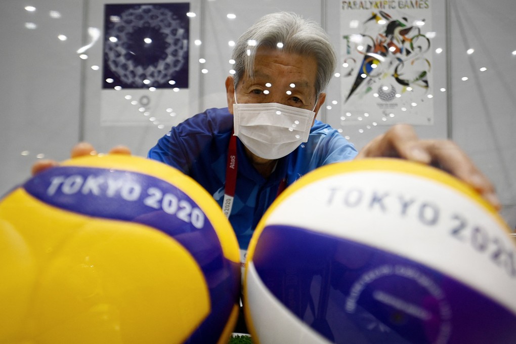 A Tokyo Olympics volunteer wearing a facemask poses with volleyballs behind a protective plexiglass plate at the media centre ahead of the opening of the Tokyo 2020 Olympic Games. Photo: AFP