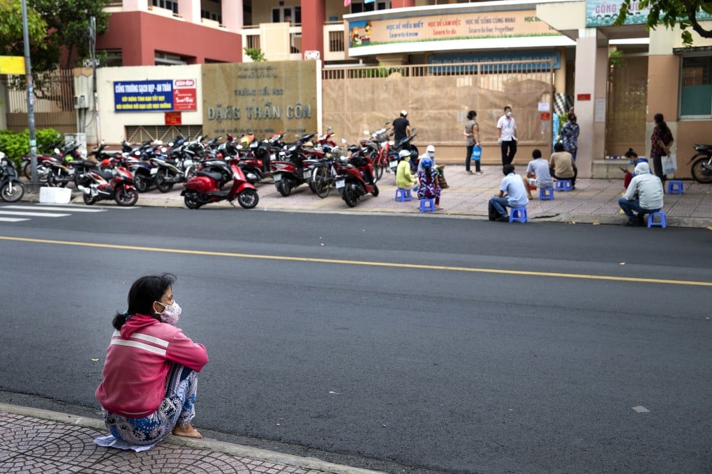 A woman sits on the pavement opposite a vaccination centre in Ho Chi Minh City, Vietnam. Authorities expect it will take months to contain the coronavirus outbreak in the region. Photo: Bloomberg