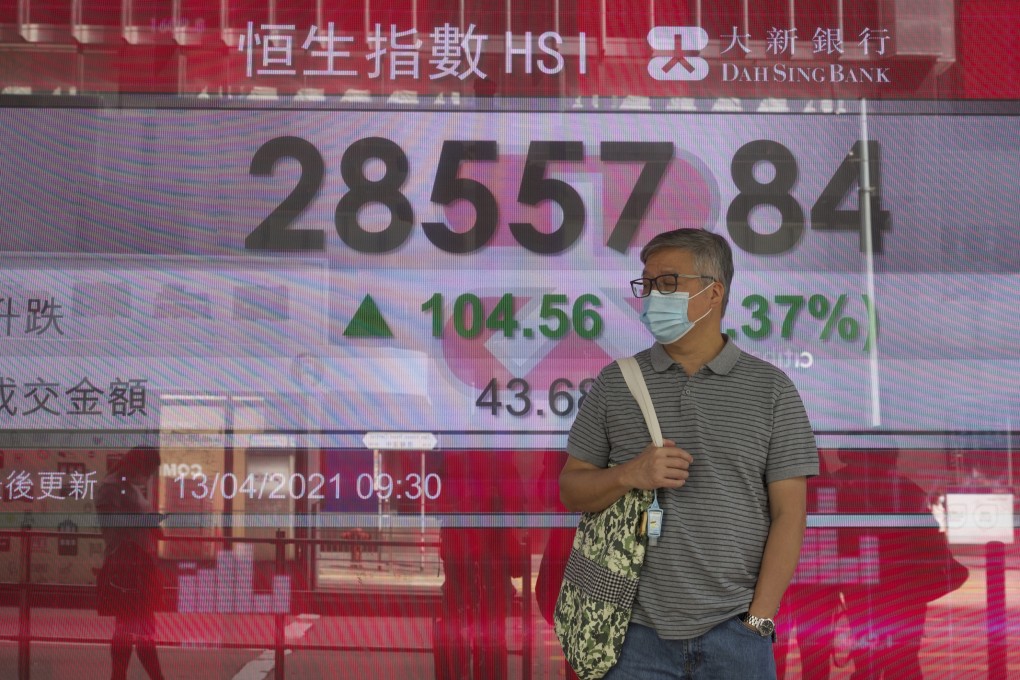 A man wearing a face mask walks past a bank's electronic board showing the Hang Seng Index in April 2021. Photo: AP