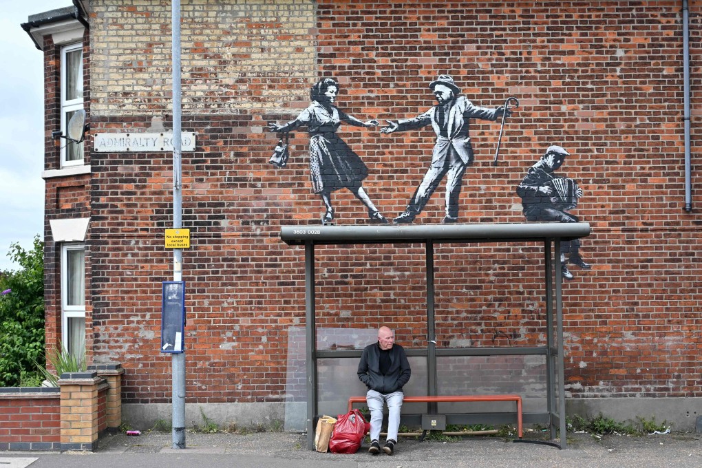 A man waits at a bus stop below a graffiti artwork of a couple dancing to an accordion player, which bears the hallmarks of street artist Banksy, on a wall in Great Yarmouth, England on August 8. Photo: AFP