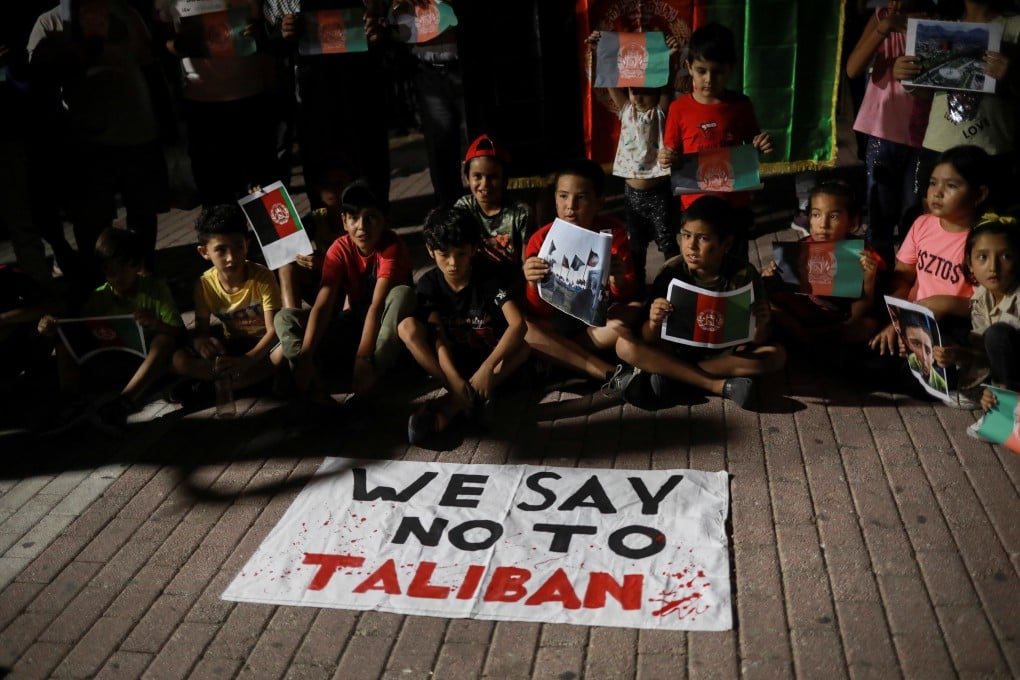 Children sit in front of a banner reading ‘We say No to Taliban’ as Afghan migrants demonstrate over the Taliban takeover of Afghanistan, on the island of Lesbos, Greece on Monday. Photo: Reuters