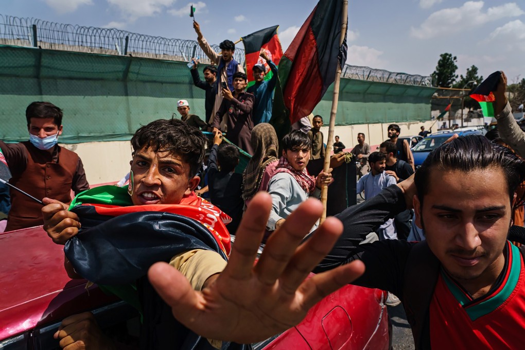 People carrying Afghanistan’s national flag march in Kabul despite the presence of Taliban fighters around them. Photo: TNS