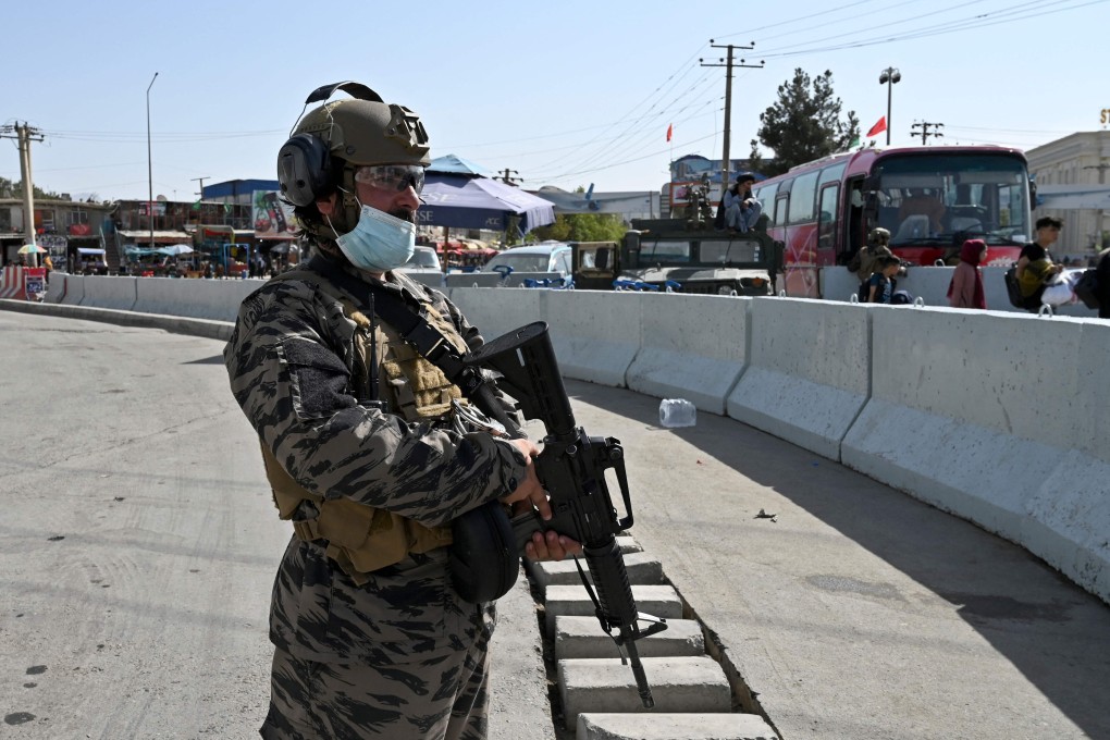 A Taliban fighter stands guard as Afghans walk to the main entrance gate of Kabul airport on Saturday. Photo: AFP