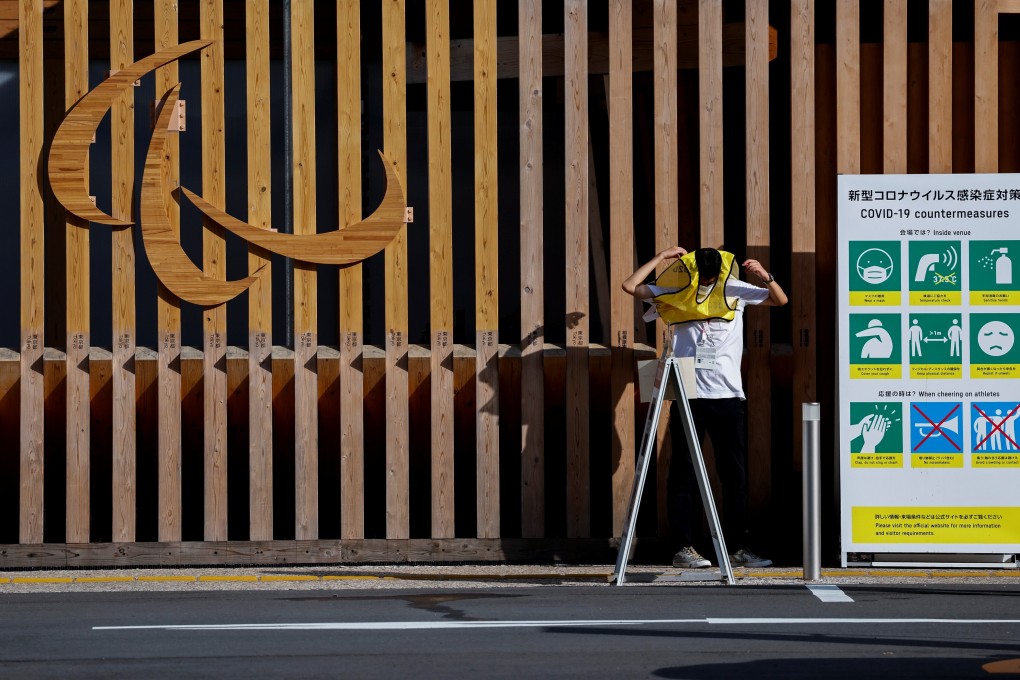 A staff member stands between the Paralympic symbol and a board advising measures against the coronavirus disease. Photo: Reuters