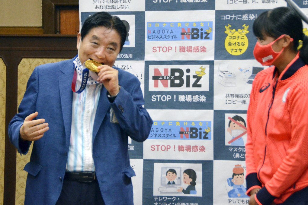 Nagoya city Mayor Takashi Kawamura bites the medal of softball athlete Miu Goto on August 4, 2021. Photo: Kyodo via Reuters