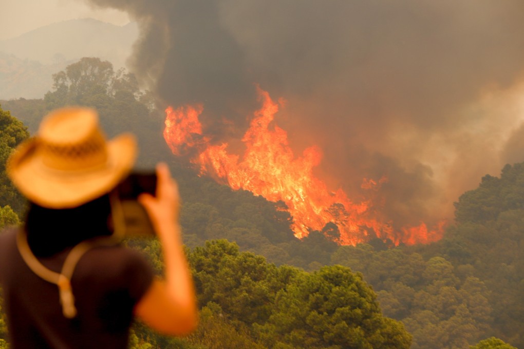 A woman takes pictures of flames as they rip through a wooded area amid forest fires in Sierra Bermeja. Photo: DPA