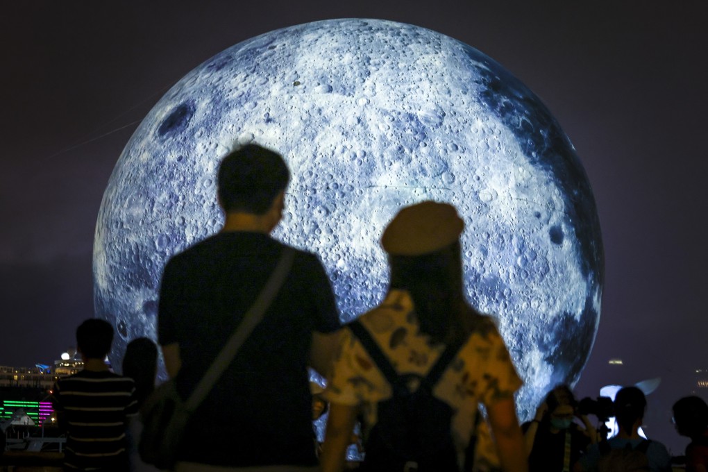 People pose for pictures against the backdrop of a huge glowing moon floating in the Kwun Tong typhoon shelter. Photo: Nora Tam