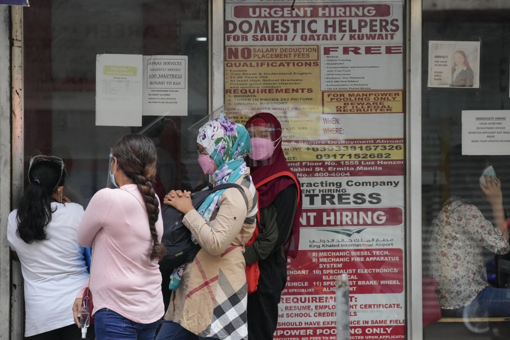 Women stand beside a sign about hiring domestic helpers for the Middle East outside an office in Manila, Philippines. Photo: AP