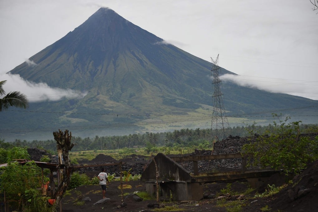 A resident of San Francisco village in Guinobatan, the Philippines’ Albay province, stands next to a house half-buried by displaced sand and rock brought from the Mayon volcano after heavy rains from last year’s Typhoon Goni. Photo: AFP