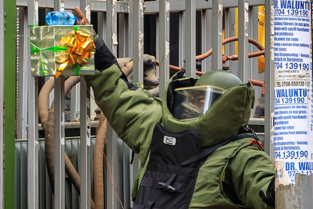 A member of the Uganda police bomb squad prepares to detonate a suspicious box wrapped with a ribbon, on a fence, in Kampala, Uganda. Photo: AFP