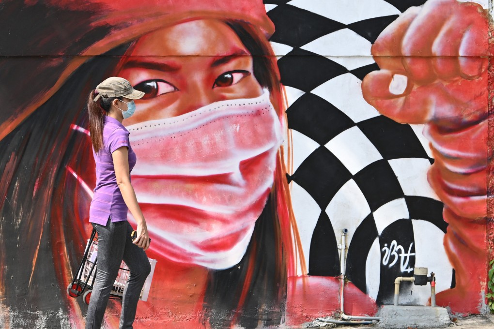 A woman walks along a street in Manila past a mural depicting health workers wearing masks. Photo: AFP