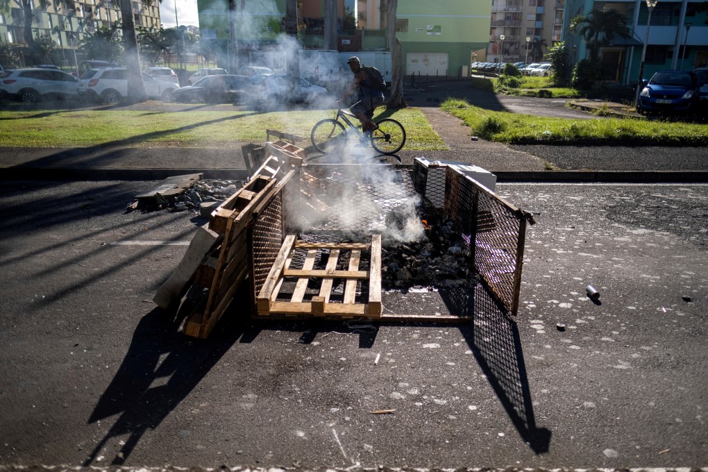 A man rides his bicycle past a smoking street barricade after violent demonstrations broke out over coronavirus restrictions in Pointe-a-Pitre, Guadeloupe on Sunday. Photo: Reuters