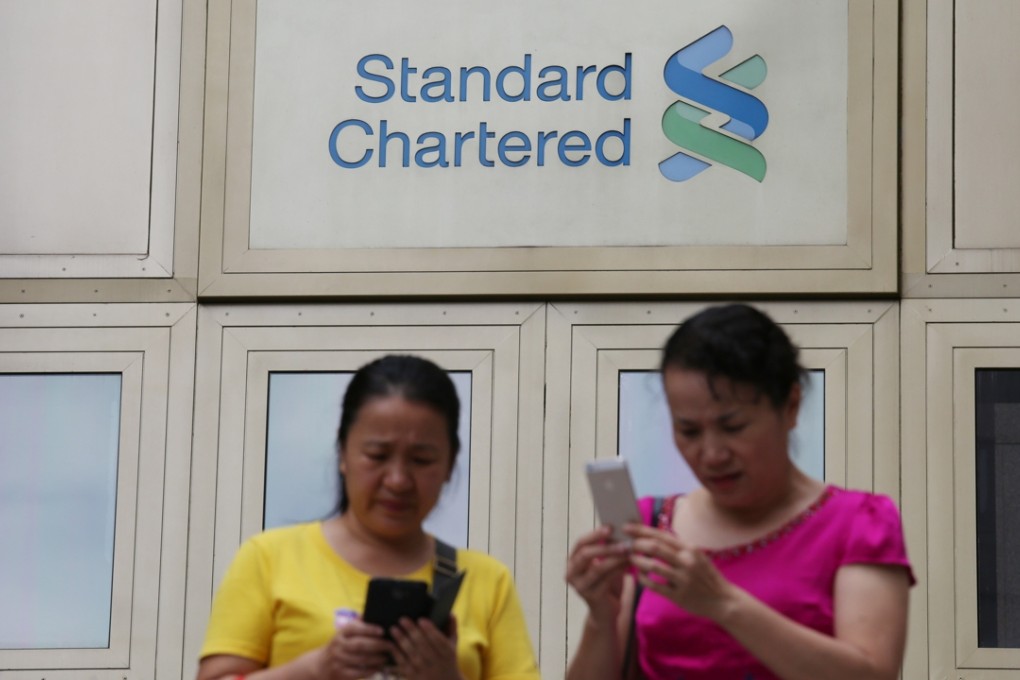 Two women browse through their cell phones underneath a signboard of the Standard Chartered Bank in Hong Kong. Photo: Nora Tam