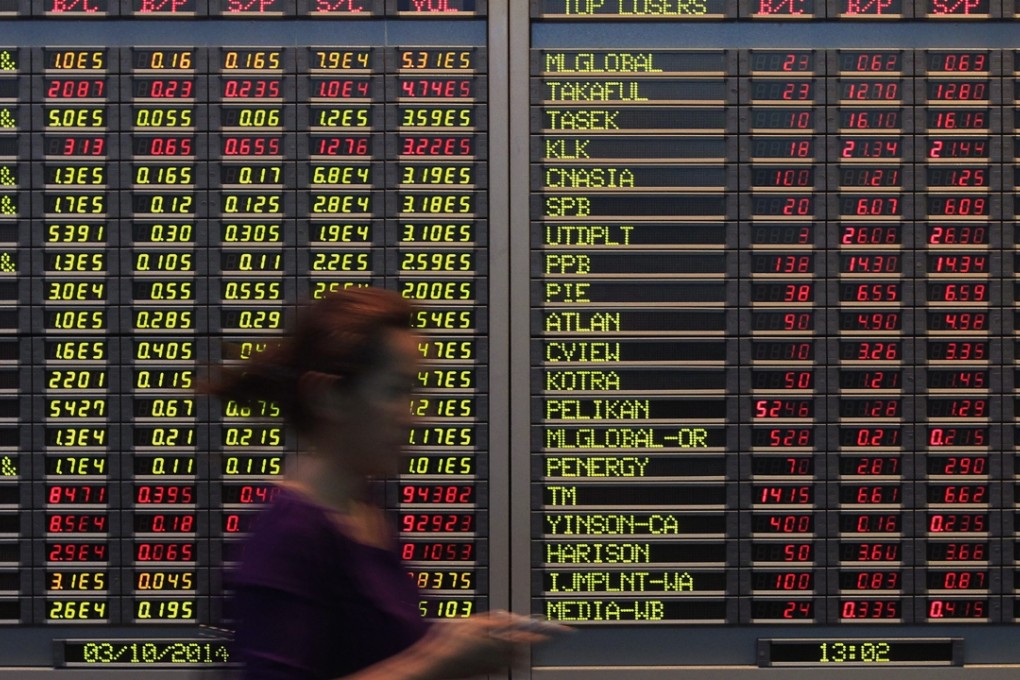 A woman walks past electronic boards showing share index at a bank in Kuala Lumpur, Malaysia. Photo: AP