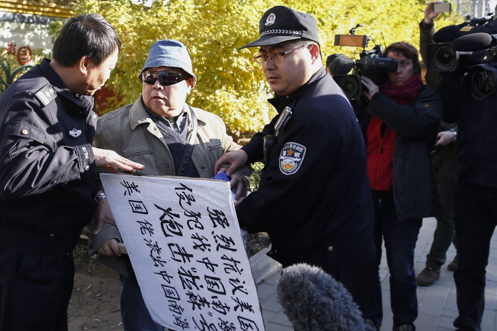 A protester with a sign that reads 'Strongly protest against US encroachment on South China Sea is held by two police outside the US Embassy in Beijing on October 28. Photo: EPA